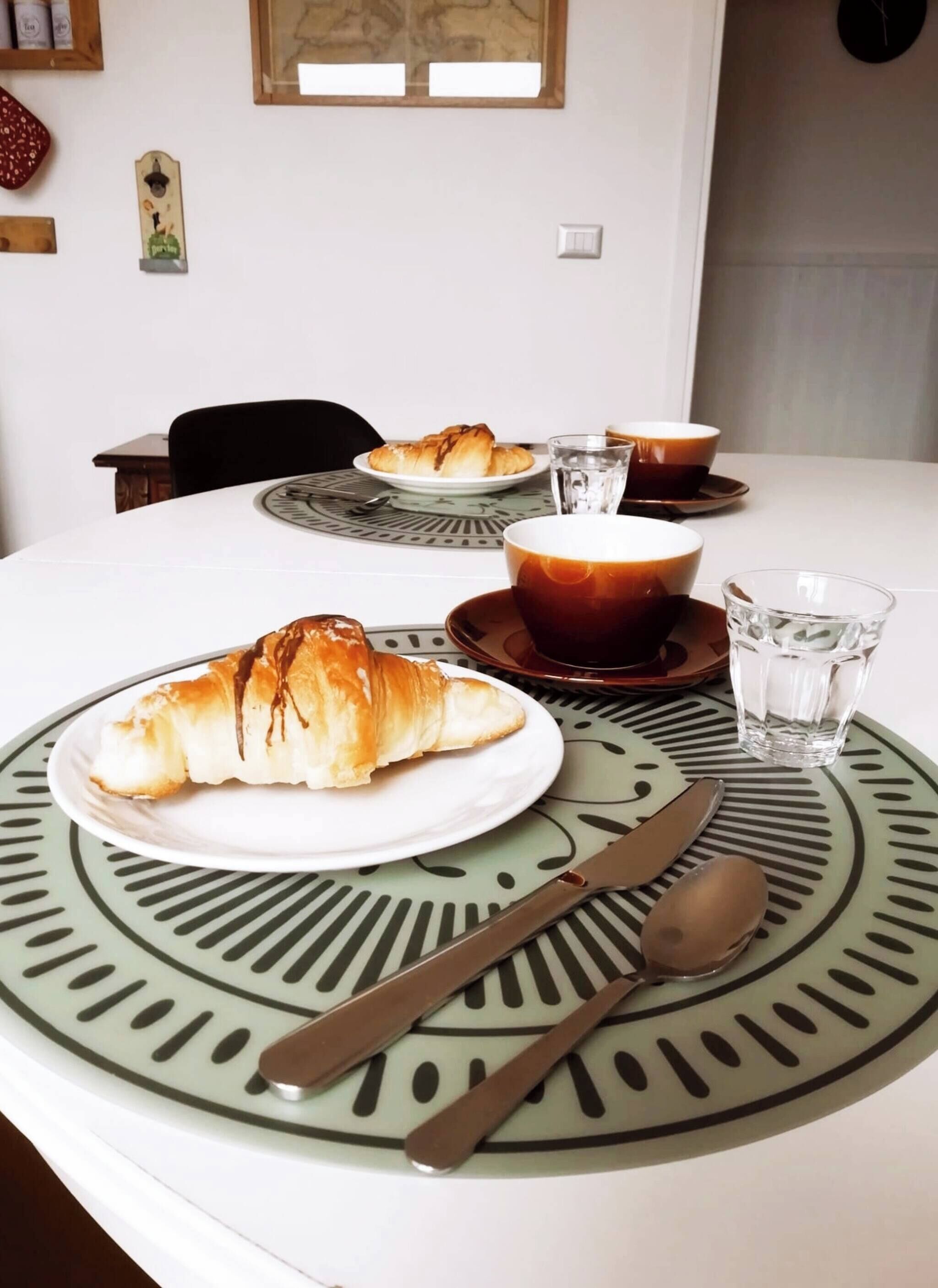 Una mesa con platos de croissants y café, una cuchara y un cuchillo.