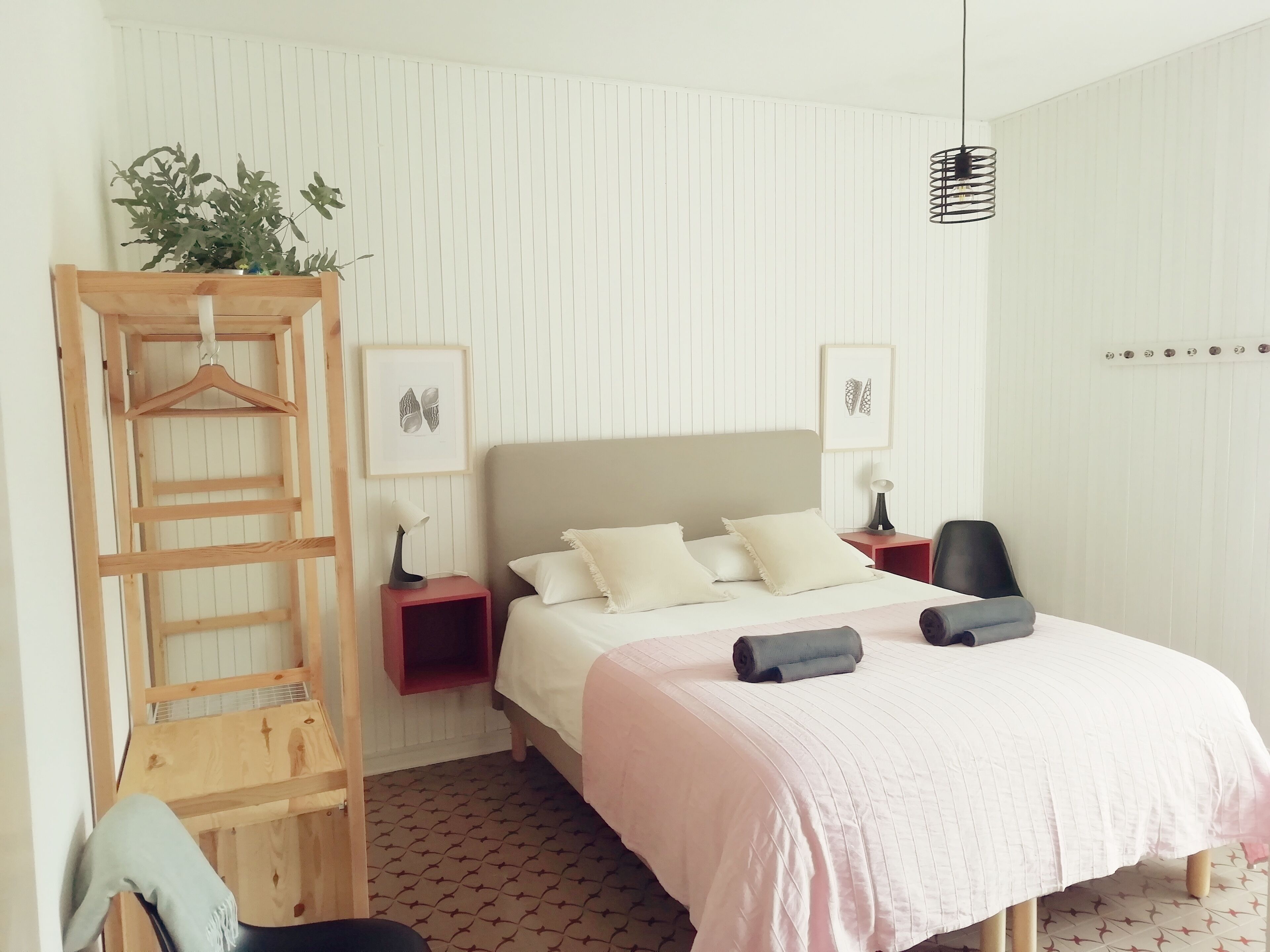 Ein Schlafzimmer mit einem Bett, einer Holzleiter, einem roten Nachttisch, einem schwarzen Stuhl und einer hängenden Deckenleuchte.