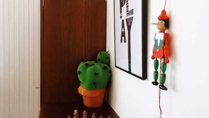 Un jeu d’échecs est installé sur une table en bois, dans une pièce dont le mur est blanc, ornée d’un tableau encadré et d’une petite figurine.