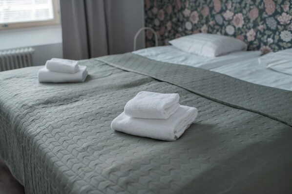 Una cama bien hecha con un edredón verde texturizado y dos toallas blancas dobladas.