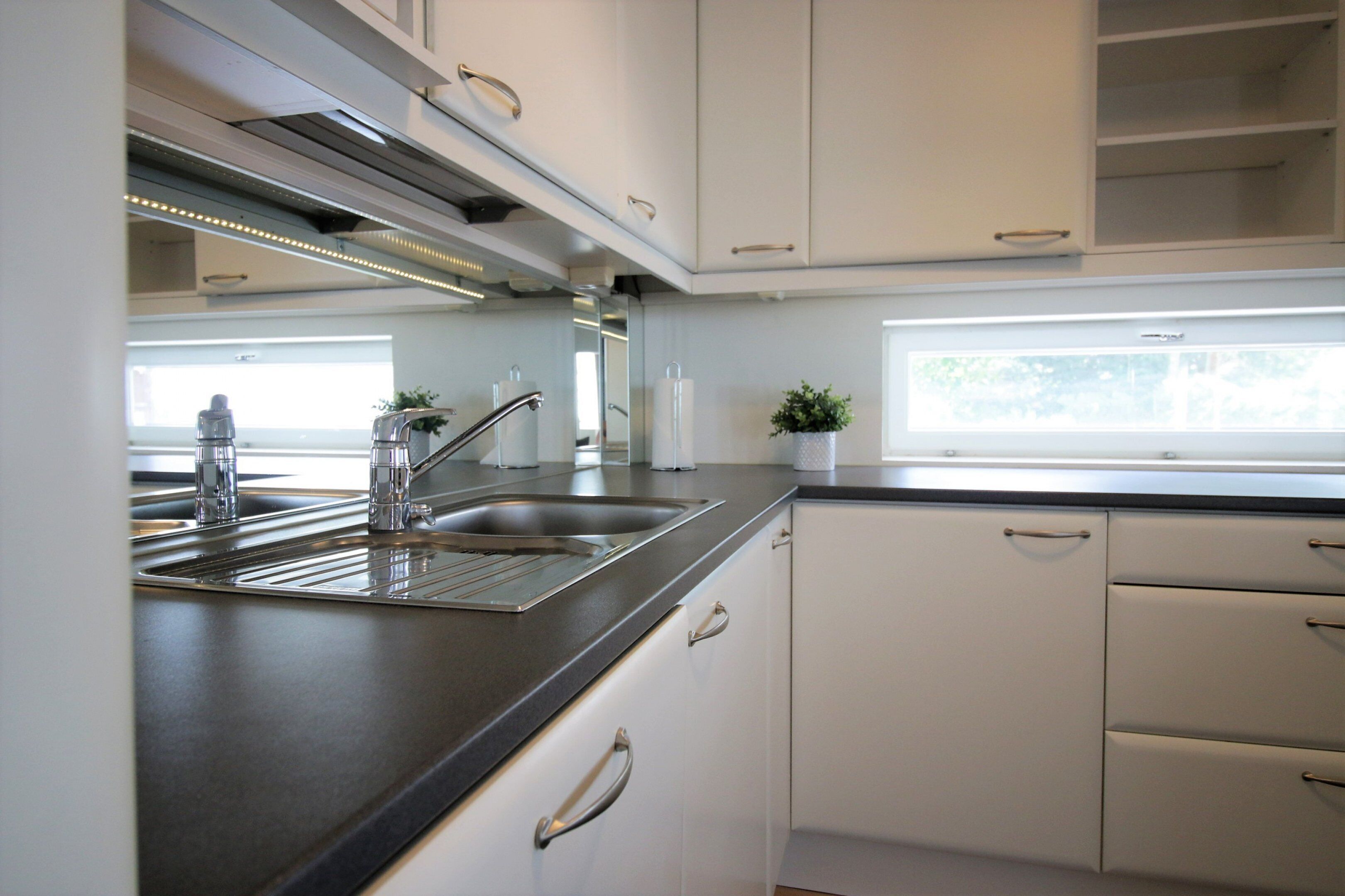 Una cocina moderna con un lavamanos de acero inoxidable, armarios blancos y una ventana que ofrece luz natural.