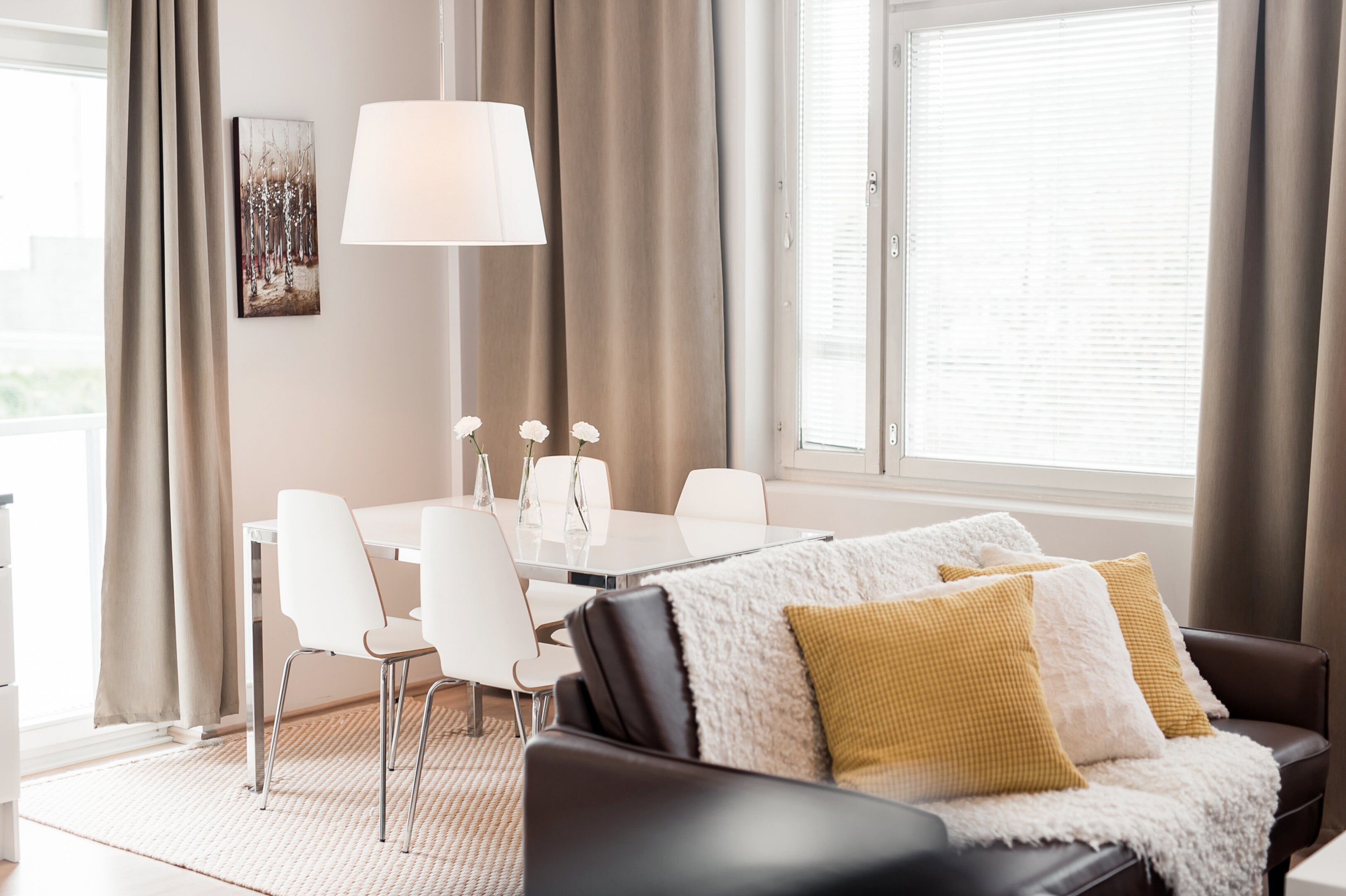 Una sala moderna con una mesa de comedor blanca, un sofá con cojines y una lámpara.