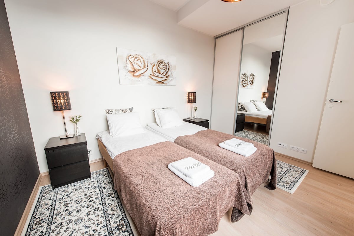 Habitación de hotel con dos camas, un espejo grande, una mesita de noche y una obra de arte colgada en la pared.
