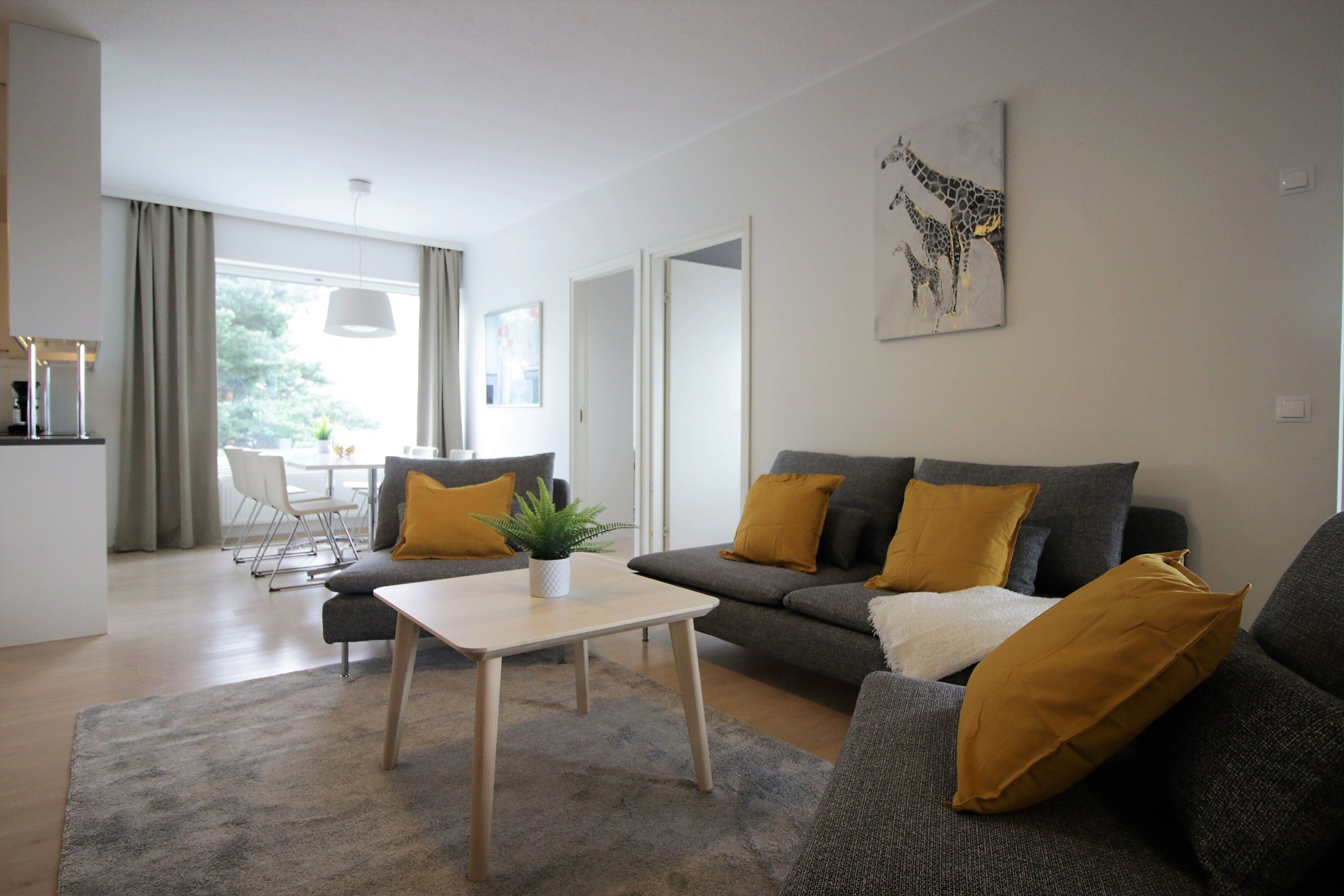 Una sala de estar moderna con un sofá gris, una mesa de centro blanca y un área de comedor al fondo.