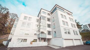 A modern multi-story building with a white facade, multiple balconies, and a gated entrance.