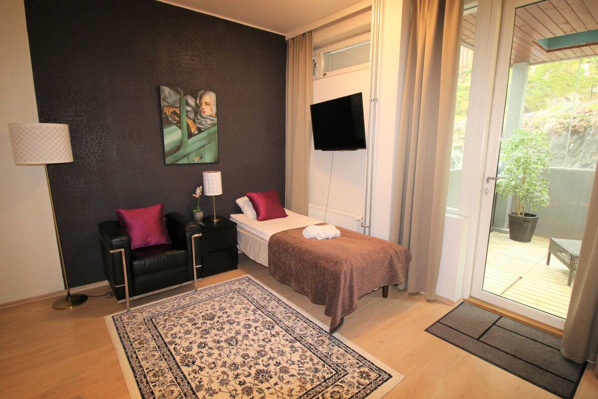 Un dormitorio con cama, televisor, sofá, alfombra y vistas al exterior.