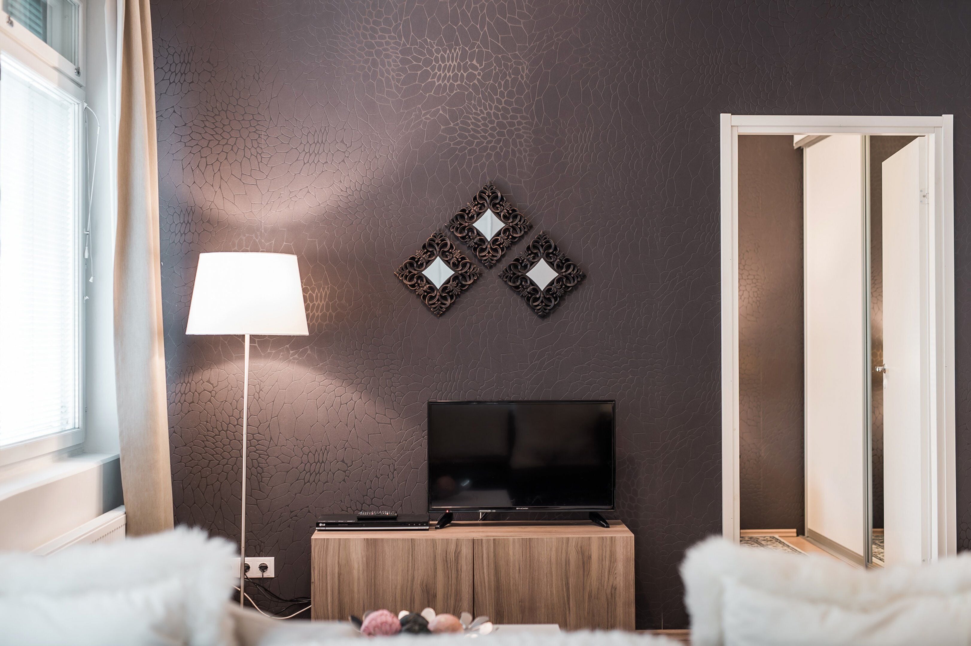 A modern living room with a flat-screen TV on a wooden stand, a floor lamp, and decorative wall art.