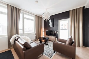 Uma sala de estar moderna com um sofá, poltronas, uma mesa de centro, televisão e um lustre.