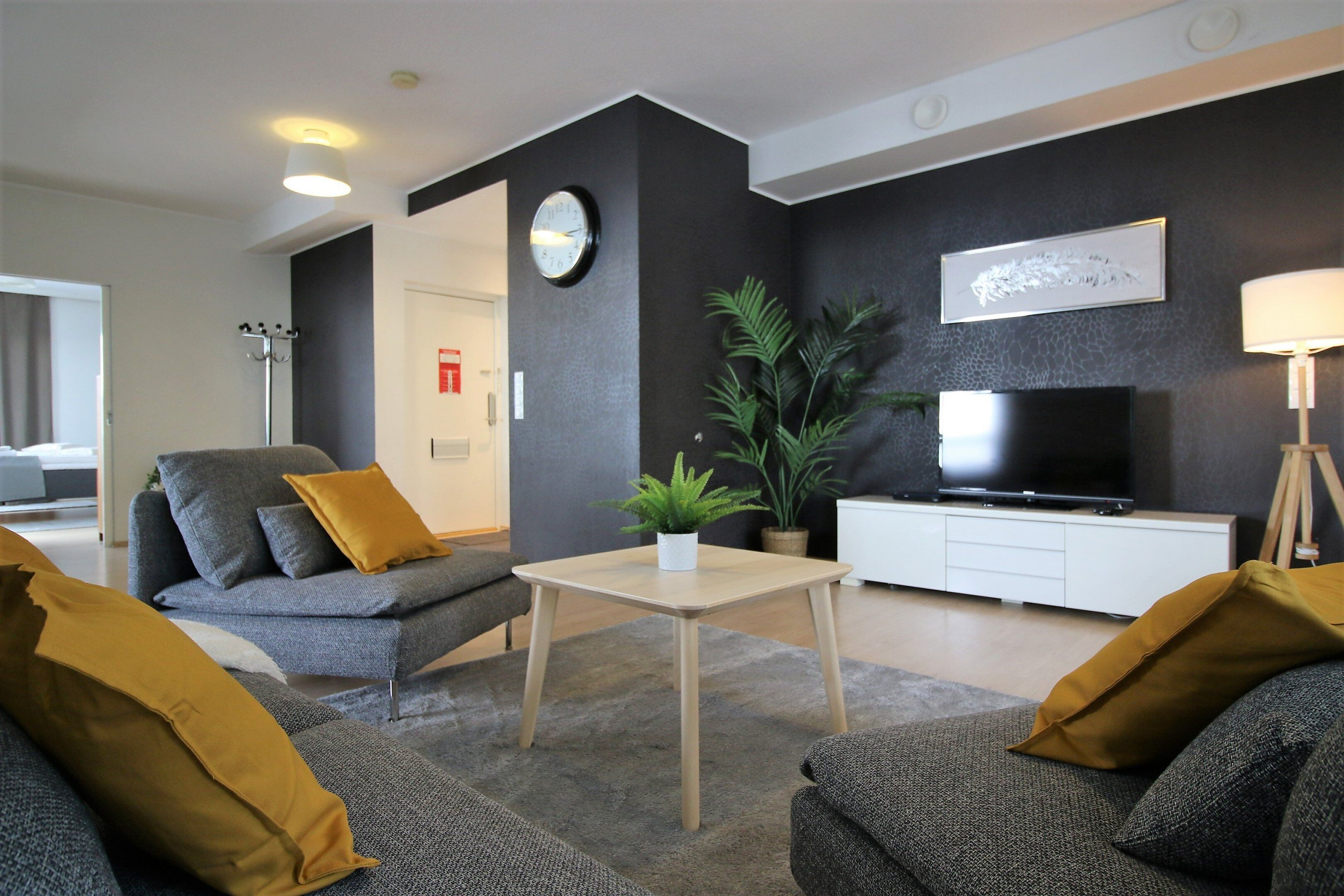 A modern living room with a grey sofa, a small table, a TV, and a plant.