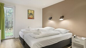 Una habitación de hotel moderna con una cama grande, una mesita de noche y un ventanal con vistas a árboles.