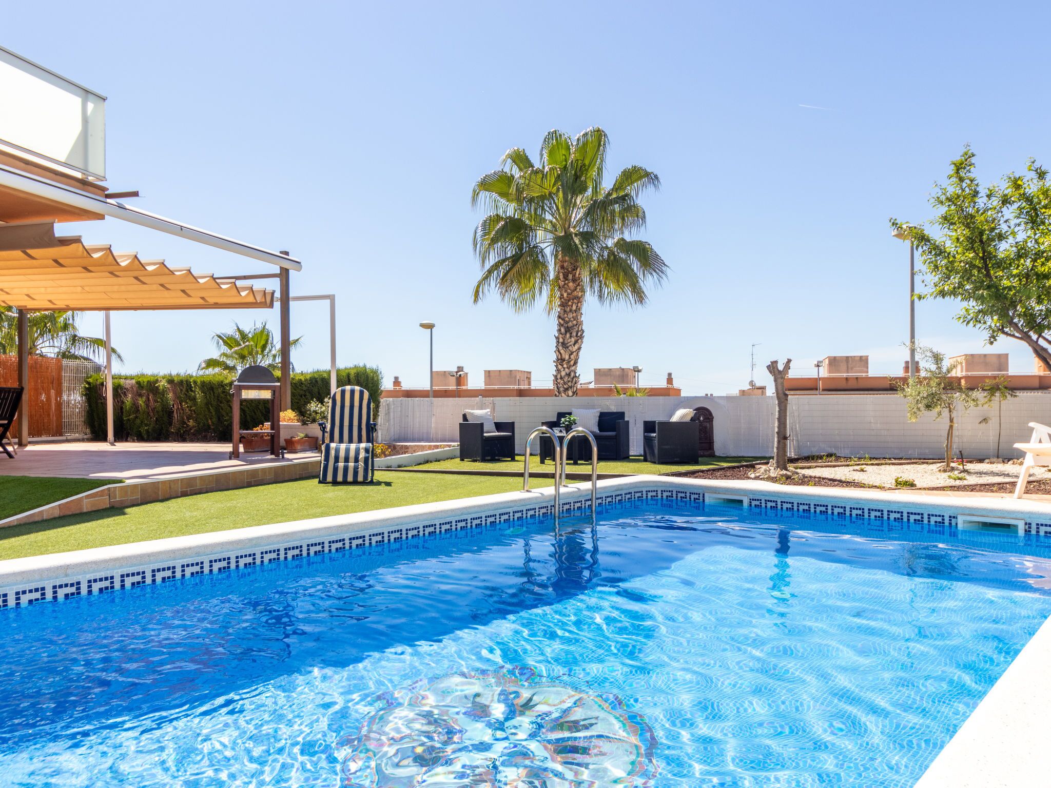 Une piscine à l’eau d’un bleu cristallin, entourée d’un patio aménagé avec des meubles d’extérieur et un palmier.