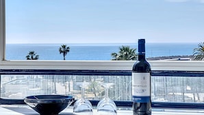 Eine Flasche Rioja-Wein, zwei Weingläser und eine schwarze Schale auf einem Tisch mit Blick aufs Meer.
