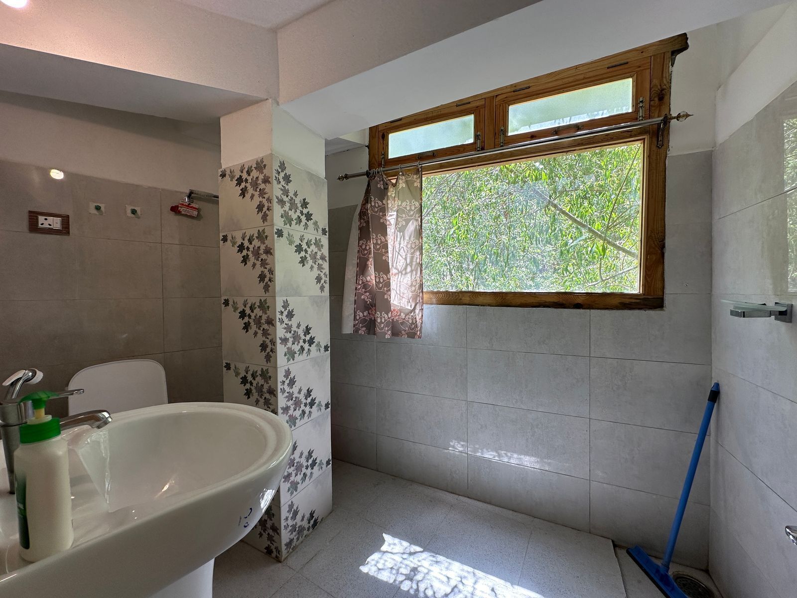 A bathroom with a bathtub, a sink, and a window with a view of greenery.