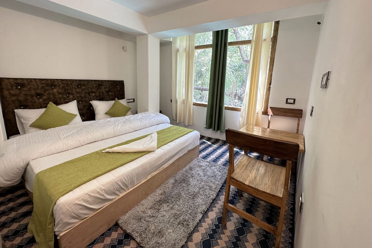 Ein Schlafzimmer mit einem großen Bett, einem Holztisch und Blick auf Bäume durch das Fenster.