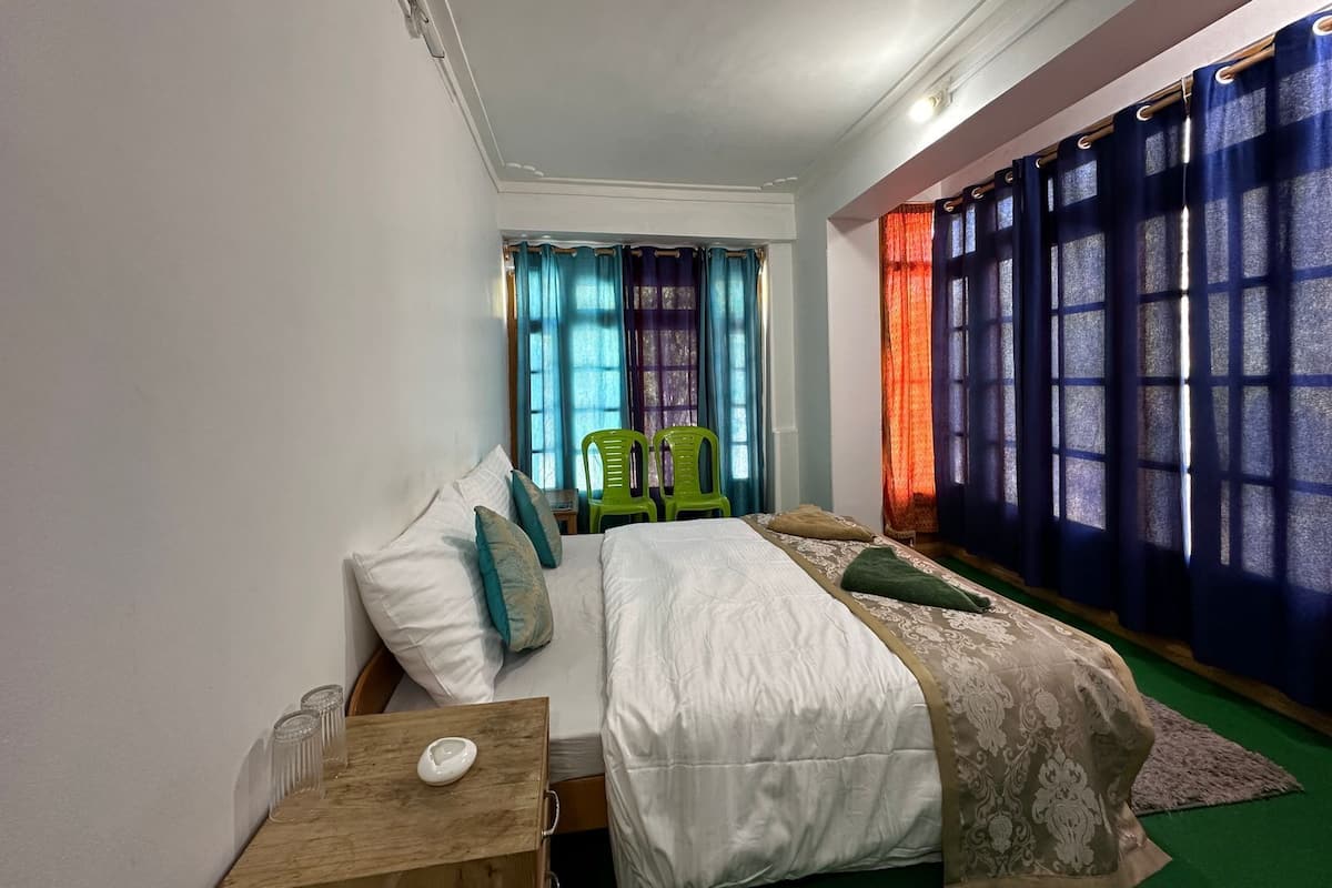 Ein Schlafzimmer mit einem Bett, zwei Stühlen, einem Nachttisch und einem Fenster mit bunten Vorhängen.