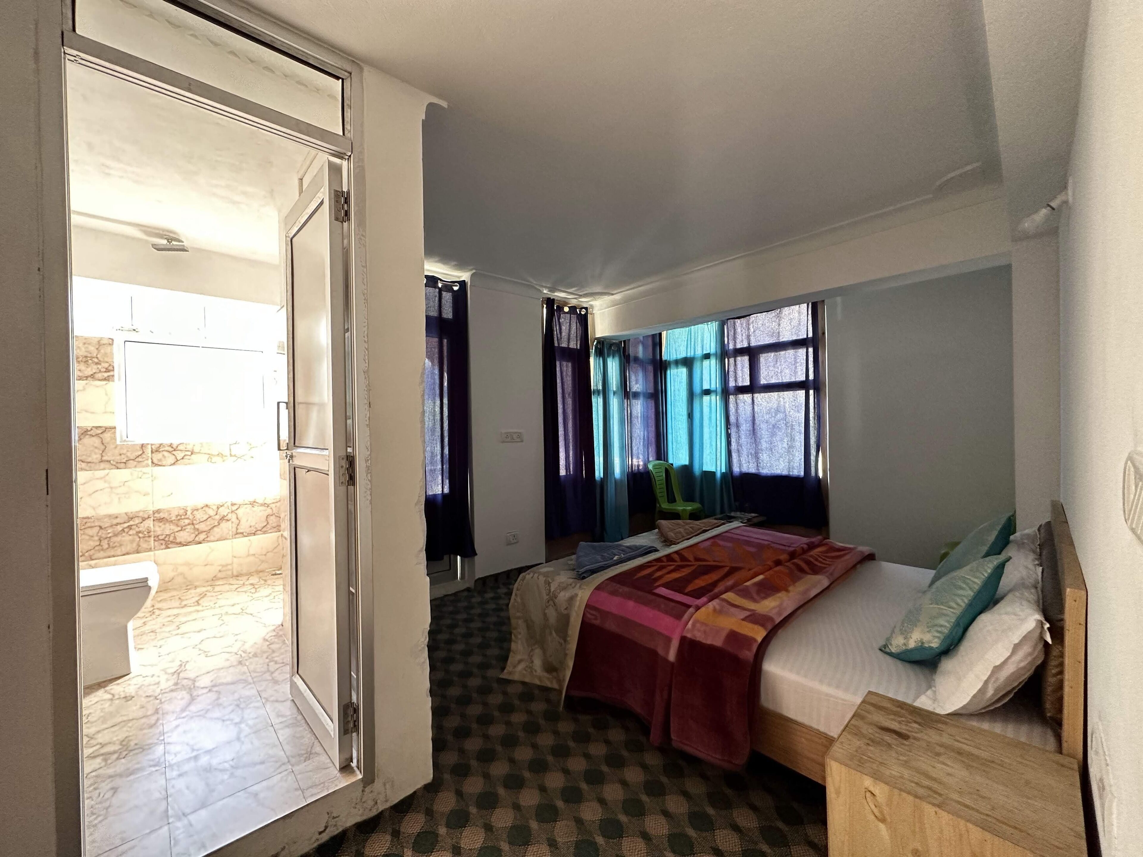 A bedroom with a bed, a chair, a window with curtains, and a door leading to another room.