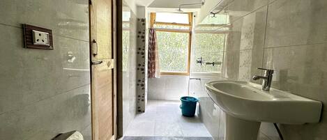 Un baño con lavamanos, ducha y ventana con cortinas.