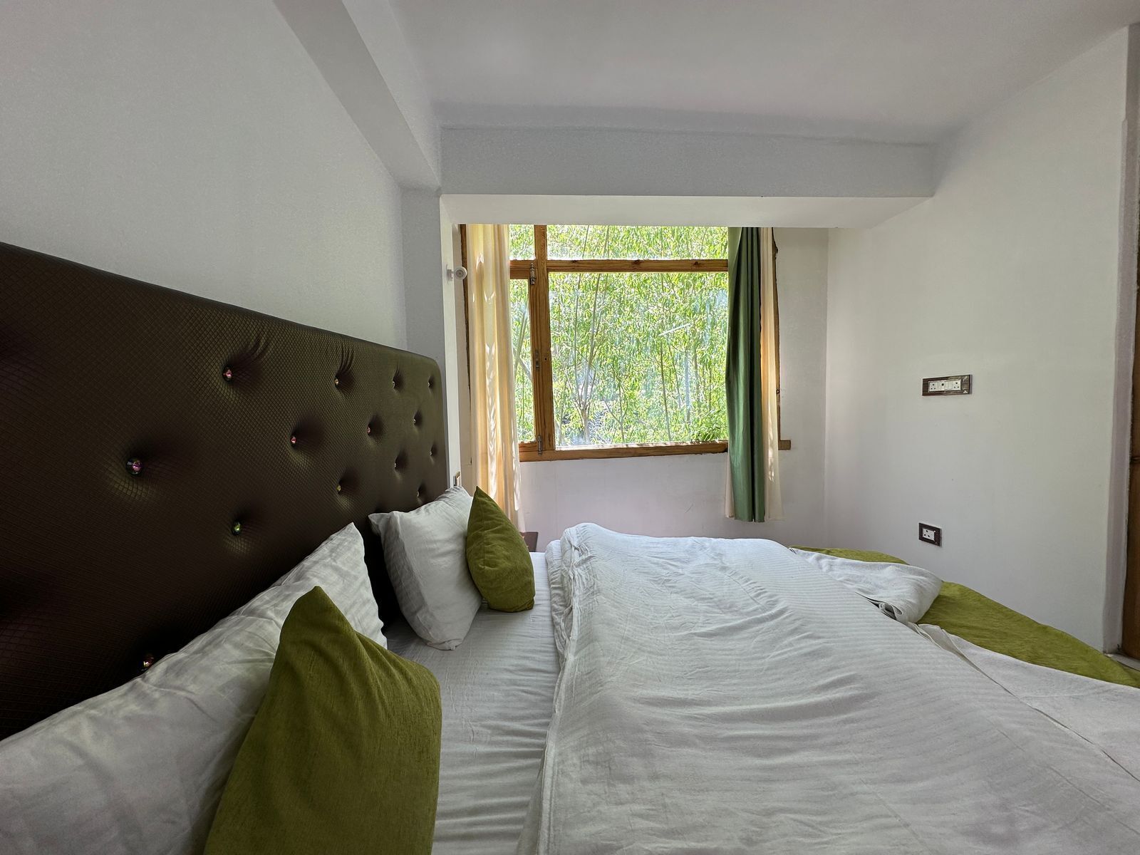 Een slaapkamer met een groot bed, een hoofdbord en een raam met uitzicht op groen.