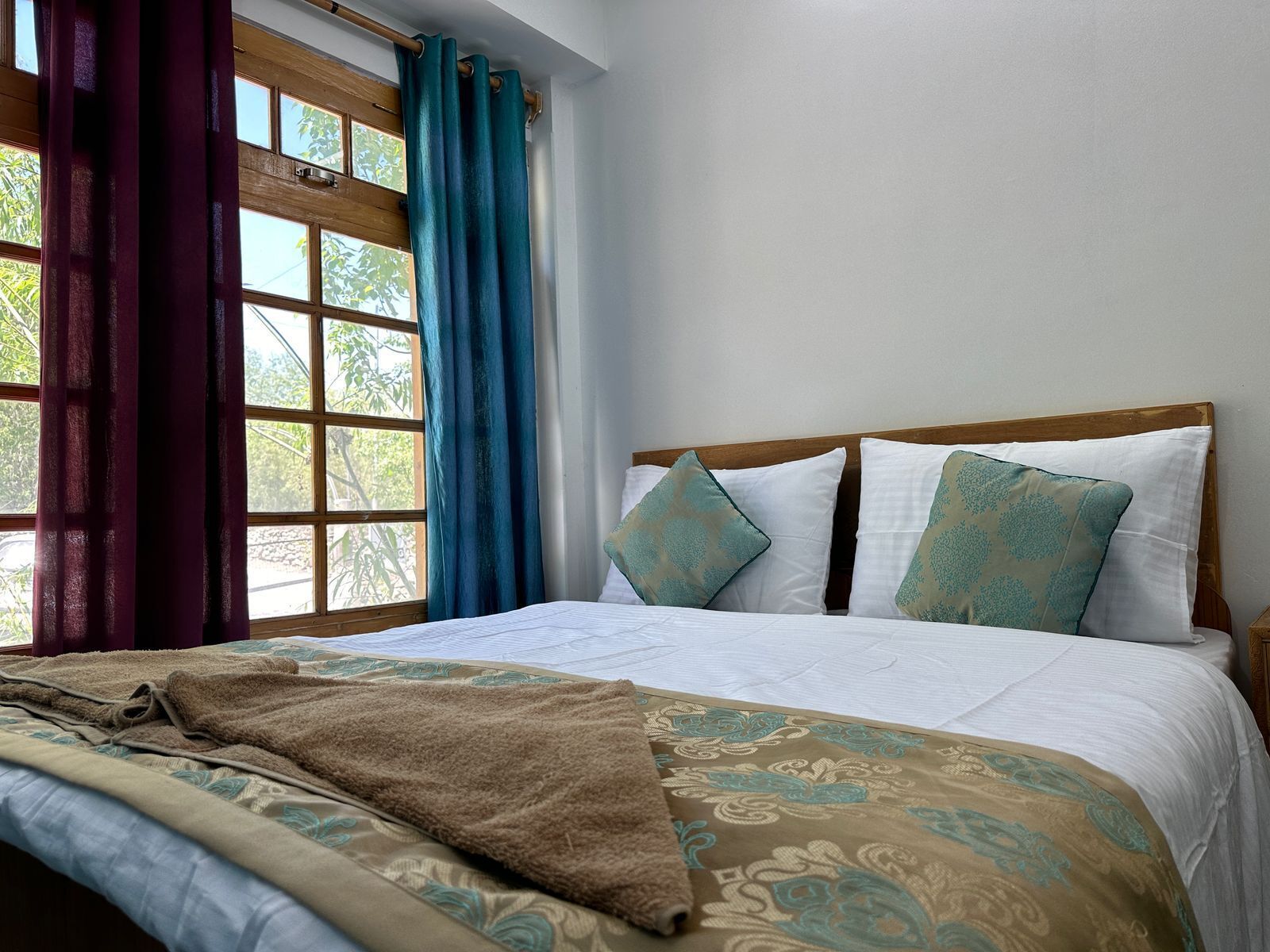 A neatly made bed with patterned bedding, a wooden headboard, and a window with curtains.