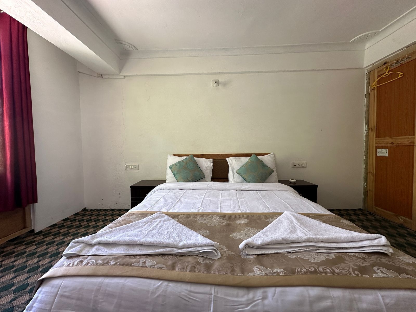 A hotel room with a bed, two nightstands, a wooden wardrobe, and a red curtain.