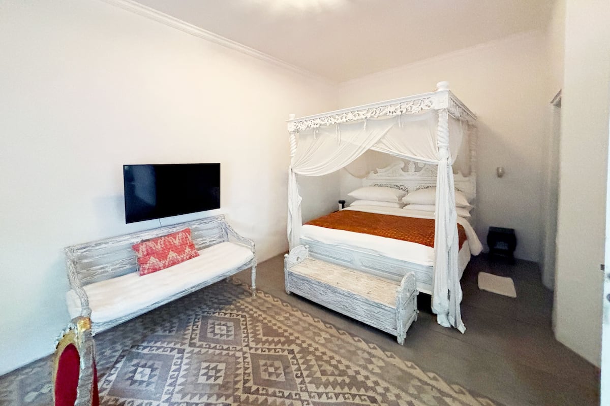 A bedroom with a four-poster bed, a TV mounted on the wall, and a patterned rug.