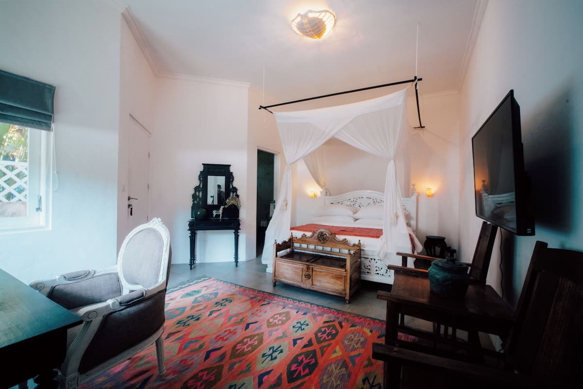 A bedroom with a four-poster bed, a wooden nightstand, a chair, a television, and a patterned rug.