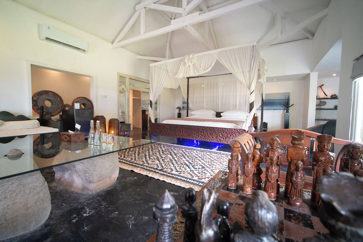 A bedroom with a four-poster bed, a glass coffee table, and a chess set.