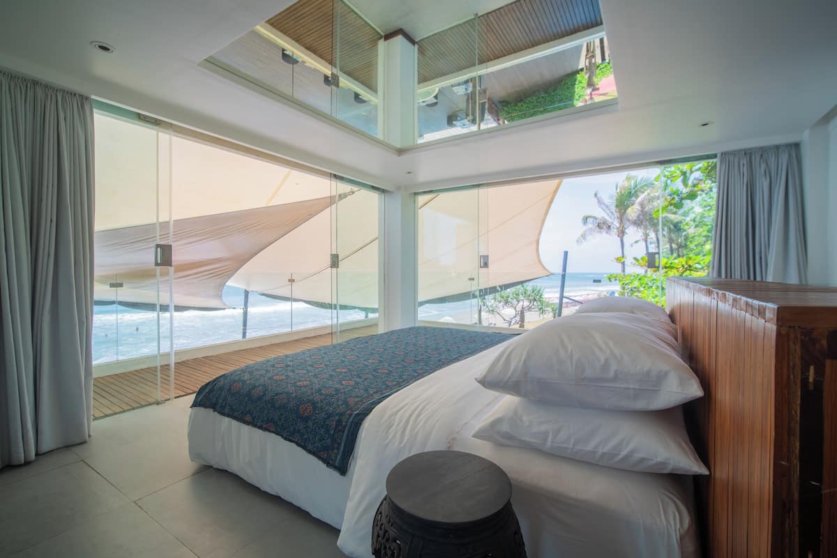 A modern bedroom with a large bed, a view of the ocean, and a balcony with a view of the beach.