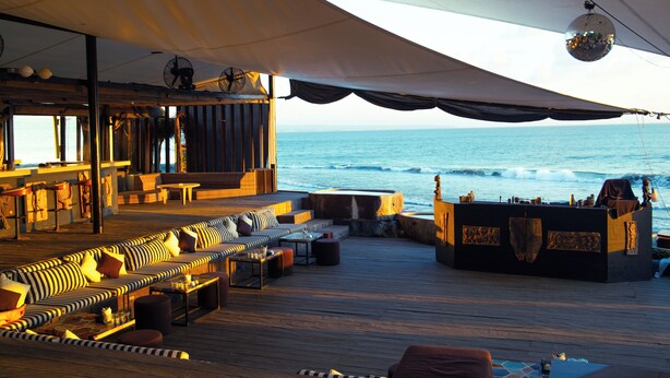 A deck with a long sofa and a bar area overlooking the ocean. - Morabito Art Villa (Tibubeneng)