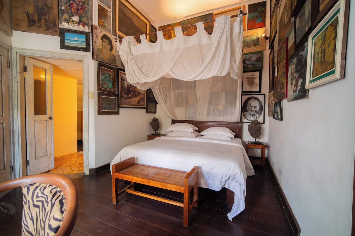 A bedroom with a canopy bed, wooden furniture, and various framed artworks on the walls.