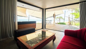 A modern room with a glass coffee table, a red sofa, and a view of the beach through large windows. - Morabito Art Villa (Tibubeneng)