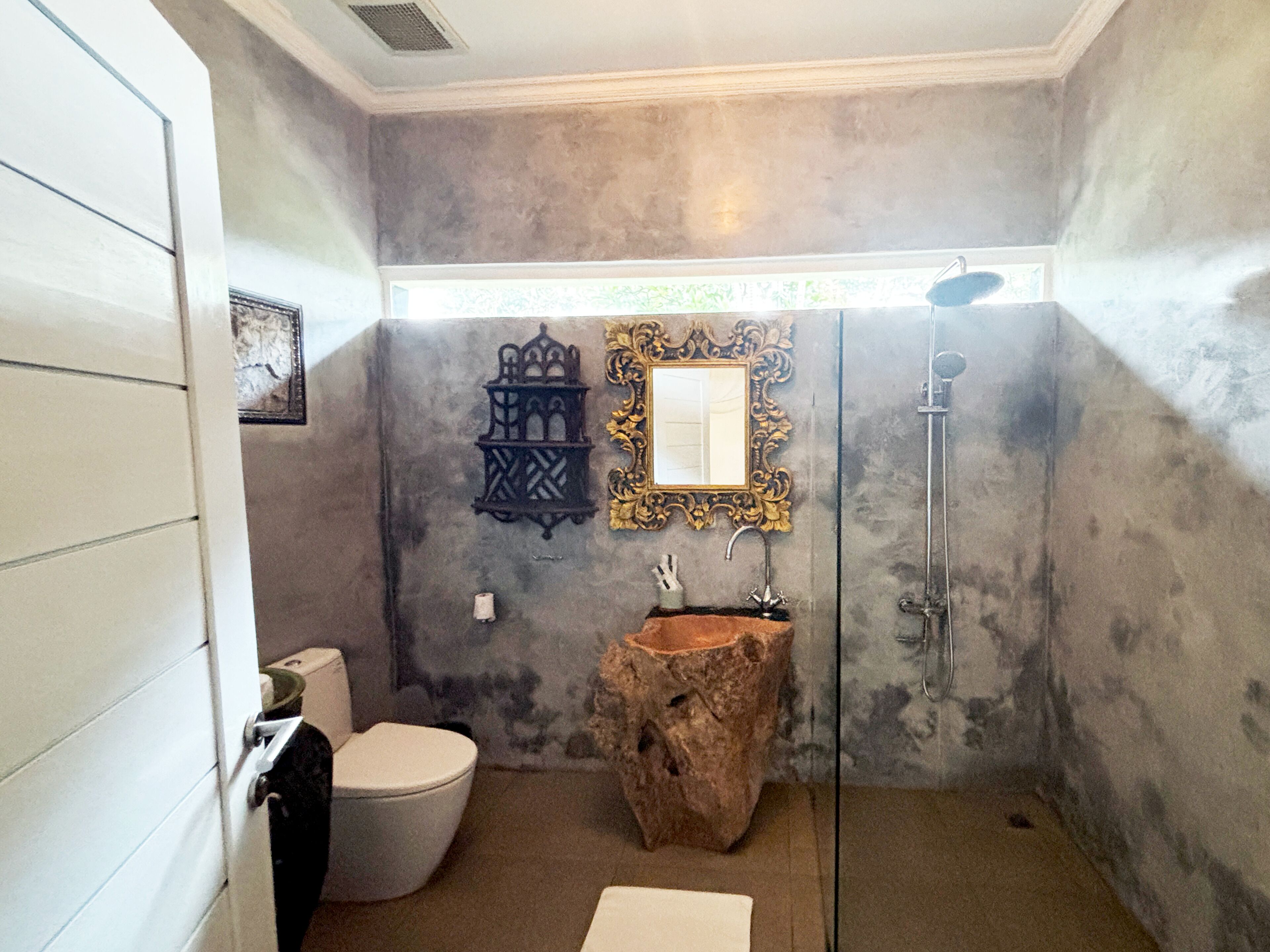 Un baño con inodoro blanco, lavabo de madera, espejo decorativo y ducha.