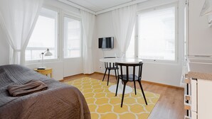A hotel room with a bed, a small table with chairs, a TV, and large windows with curtains. - Forenom Apts Turku Laukkavuori (Turku)