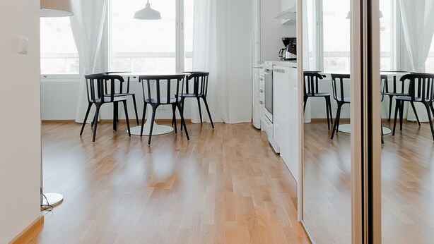 A spacious, modern living area with a wooden floor, white walls, and a large sliding glass door leading to a balcony. - Forenom Apts Turku Laukkavuori (Turku)