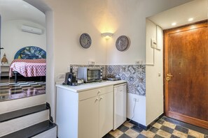 A compact kitchen with a microwave, coffee maker, and a small refrigerator. There is a wooden door and a tiled floor. - La Finestra Sul Giardino in Sanremo (Sanremo)