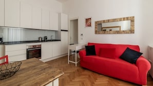 A modern kitchen with white cabinets, a red sofa, and a wooden dining table. - Piazza Vittorio Luxury House (Roma)