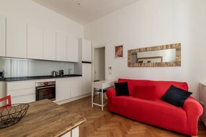 A modern kitchen with white cabinets, a red sofa, and a wooden dining table.