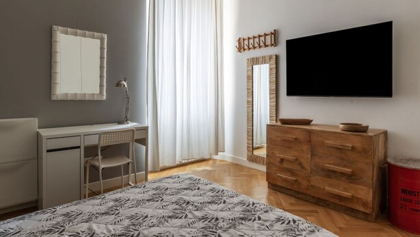 A bedroom with a bed, a desk, a chair, a dresser, a TV, and a window with curtains. - Piazza Vittorio Luxury House (Roma)