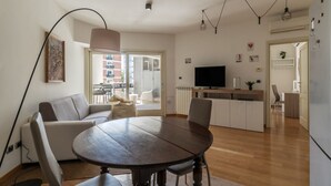 Un espacio de estar moderno con mesa de comedor, sofá, televisor y zona de cocina.