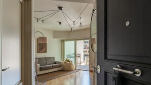 Un interior moderno con un sofá, un sillón informal y un comedor visible a través de una puerta de cristal.