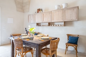 A dining area with a wooden table, wicker chairs, and a cabinet above with kitchenware.