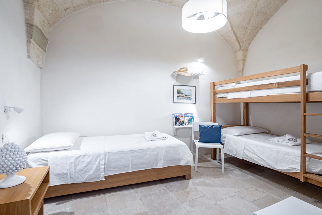 A room with a bunk bed, a single bed, a desk with a lamp, and a chair.