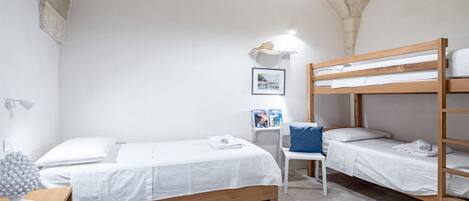 A room with a bunk bed, a single bed, a desk with a lamp, and a chair.