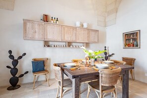 Ein Essbereich mit einem Holztisch, Korbstühlen, einer Kaktusskulptur und einem an der Wand befestigten Schrank mit Flaschen.