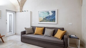 Een moderne woonkamer met een grijze bank, gekleurde sierkussens, een lijst met abstracte kunst en een bijzettafeltje.
