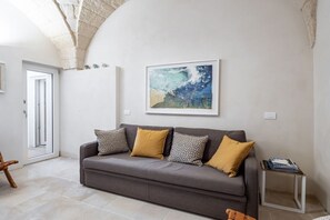 Ein modernes Wohnzimmer mit grauem Sofa, gemusterten Kissen, einem gerahmten abstrakten Gemälde und einem kleinen Beistelltisch.