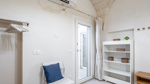 Een kamer met een witte bank, een witte plank met manden, een deur met een ruit en een airconditioner.