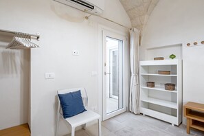 A room with a white bench, a white shelf with baskets, a door with a glass panel, and an air conditioning unit.