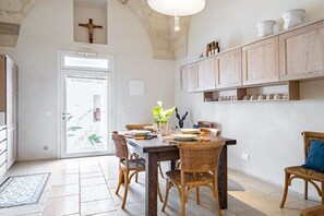 Ein Essbereich mit einem Tisch, gedeckt für vier Personen, umgeben von Korbstühlen, einem Holzschrank darüber und einem Kreuz an der Wand.