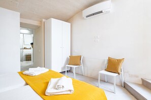 Ein Hotelzimmer mit einem Bett, zwei Stühlen, einem gelben Handtuch, einem weißen Kleiderschrank und einer Klimaanlage.